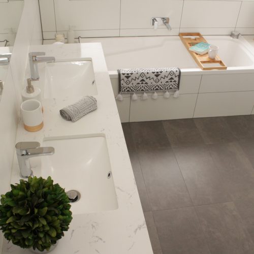 White stone top vanity with bamboo bath caddy and grey tiles